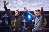 Liam og Noel Gallagher står på scene med armene løftet foran publikum i Toronto.