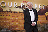 Sir David Attenborough i svart smoking står foran en Our Planet-vegg med Netflix-logoer.