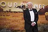 Sir David Attenborough i svart smoking står foran en Our Planet-vegg med Netflix-logoer.
