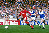 Kenny Dalglish i rødt løper med ballen foran to Everton-spillere på gressbanen.