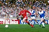 Kenny Dalglish i rødt løper med ballen foran to Everton-spillere på gressbanen.