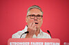 Sir Keir Starmer speaking behind a podium with a red backdrop in London.