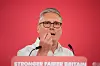Sir Keir Starmer speaking behind a podium with a red backdrop in London.