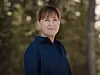 Kvinne i mørk blå skjorte står utendørs foran en uskarp skogsbakgrunn.