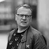 Svart-hvitt-portrett av en mann med briller og jakke mot uskarp bakgrunn.