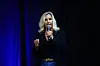 Erin Brockovich speaks into a microphone on a dark stage with blue lighting.