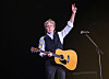 Paul McCartney står på scenen med gitar og hevet arm under en konsert på Glastonbury.