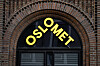 Gult OsloMet-skilt over en buet inngang i en rød murfasade.