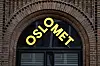 Gult OsloMet-skilt over en buet inngang i en rød murfasade.