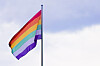 Regnbuefarget prideflagg vaier på en flaggstang mot lys himmel.