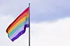 Regnbuefarget prideflagg vaier på en flaggstang mot lys himmel.