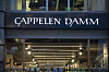 Fasadeskilt med Cappelen Damm i Oslo sentrum, med lys inne i lokalet.