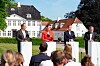 Fire politikere står ved talerstoler foran publikum utenfor en hvit bygning på Marienborg.