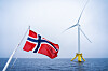Norsk flagg foran en flytende havvindmølle ute på havet.