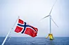 Norsk flagg foran en flytende havvindmølle ute på havet.