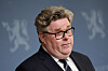 Svensk justisminister Gunnar Strömmer foran blå bakgrunn med riksvåpenmotiv.