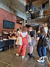 Flere personer står i kø ved en resepsjon i en lobby med mursteinvegger og høyt tak.