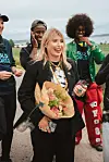 Kvinne med blomsterbukett står foran tre personer utendørs ved vannet.