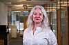 Kvinne i hvit skjorte står foran glassvegger i et lyst kontor.