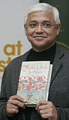 Amitav Ghosh holder opp boken «Sea of Poppies» foran et bakteppe på et mediearrangement.