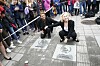 Liv Ullmann og Jakob Oftebro kneeler ved to inngravde plater i en gågate omgitt av publikum.