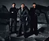Tre medlemmer av Roc Boyz står i mørke klær foran en dramatisk, grå og industriell bakgrunn.