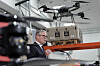 Keir Starmer taler ved en talerstol i en hangar med en drone og annet utstyr i bakgrunnen.
