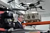 Keir Starmer taler ved en talerstol i en hangar med en drone og annet utstyr i bakgrunnen.