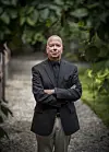 Jan Kjærstad står med armene i kors på en grussti foran grønt løvverk.