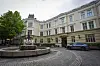 Aschehougs forlagsbygg i Oslo med fontene foran og parkert bil på brosteinsplass.
