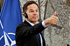 Mark Rutte gestikulerer med tommel opp under en pressekonferanse foran et Nato-flagg.