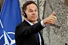 Mark Rutte gestikulerer med tommel opp under en pressekonferanse foran et Nato-flagg.