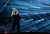 Bonnie Tyler sings onstage in black outfit beneath blue spotlights during Eurovision rehearsal.