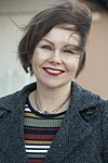 Smilende Sanna Sarromaa i mørk kåpe og stripete topp fotografert utendørs.