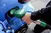 Nærbilde av en hånd som fyller drivstoff på en blå bil ved en bensinstasjon.