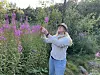 Kvinne i hage undersøker rosa blomster blant frodige planter.