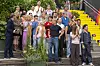 Stor gruppe Skal vi danse-deltakere poserer på utendørstrapper med fargerike klær og grønne planter.