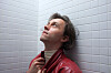 Sondre Lerche i rød skinnjakke ser opp mot taket foran en lys flisvegg.