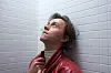 Sondre Lerche i rød skinnjakke ser opp mot taket foran en lys flisvegg.