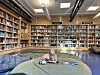 Barn ligger på et rundt teppe i et bibliotek med bokhyller i bakgrunnen.
