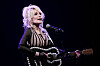 Dolly Parton synger i mikrofonen og spiller gitar på en mørklagt scene.