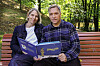 Torill Kove og Henrik Hovland viser fram en Johannes Jensen-bok på en benk i en grønn park.