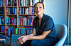 Maria Navarro Skaranger sitter i en stol foran en bokfylt hylle og holder en bok.