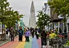 Mennesker i en regnbuefarget gågate i Reykjavik, med Hallgrímskirkja synlig mellom bygningene.
