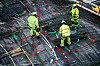 Tre arbeidere i neongrønne klær arbeider på et armeringsdekke sett ovenfra.