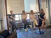Fire personer sitter i et panel foran skjermer med presentasjoner.