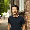Mann i svart t-skjorte står ved en rød murvegg i en urban gate.