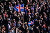 Folkemengde på rally i Reykjavik med flere islandske flagg hevet over menneskene.