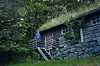 Person på trappen til en gammel tømmerhytte i frodig skog.