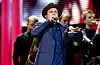 Timbuktu synger i mikrofon iført hatt og mørk jakke, med musikere på scenen bak seg.